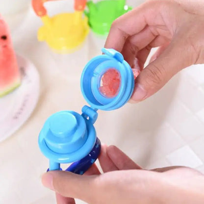 Blue container with a lid being opened, revealing a red fruit inside, with colorful objects in the background.