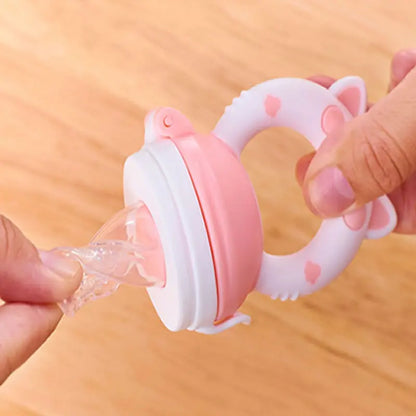 Pink and white silicone teething ring with water being poured into it on a wooden surface.