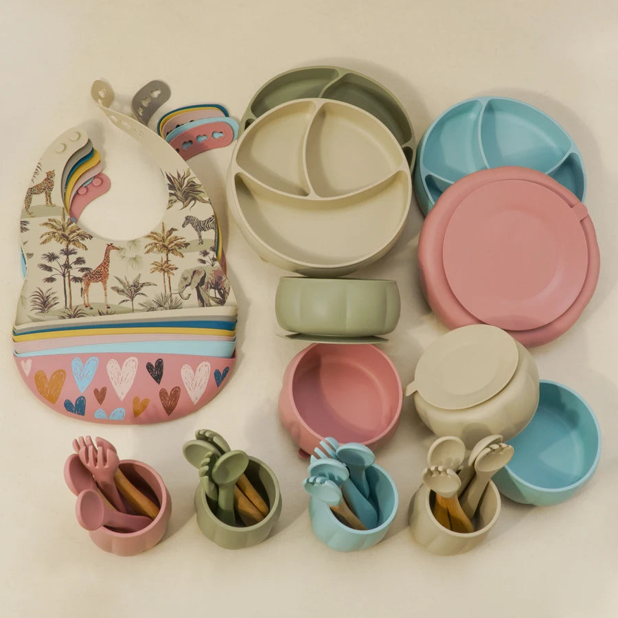 Set of colorful children's tableware including plates, bowls, and utensils on a light background