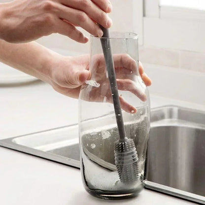 Person cleaning a glass bottle with a brush in a kitchen setting