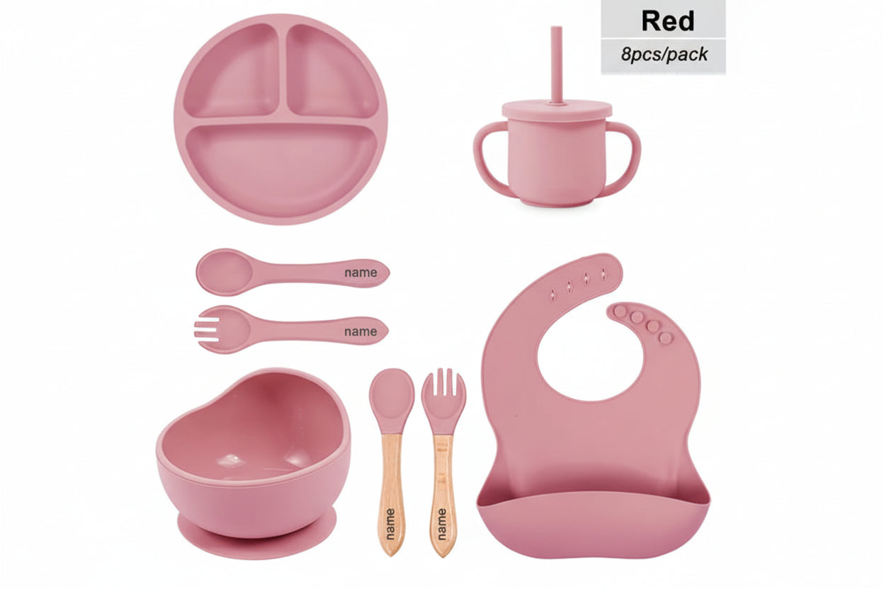 Pink children's dining set with various items including a bowl, cup, spoon, and bib on a white background.