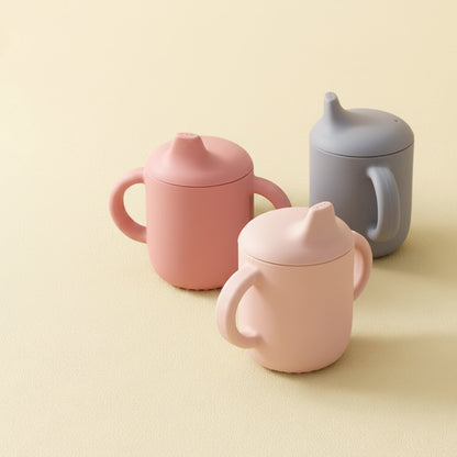 Set of colorful sippy cups on a beige background