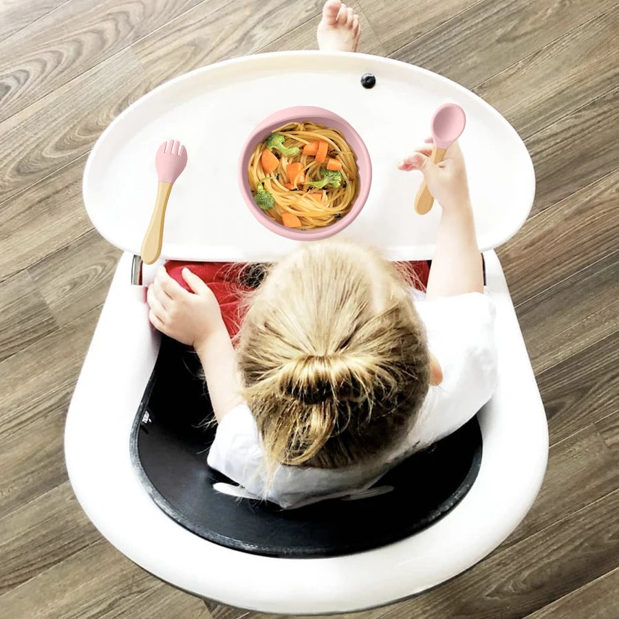 Child sitting in a white baby seat with a tray of food on a wooden floor
