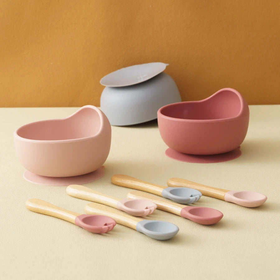 Set of pink and gray bowls and spoons on a beige surface with a brown background