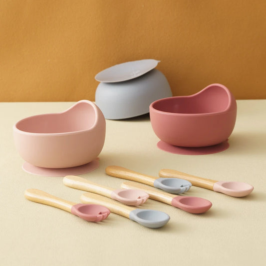 Set of pink and gray bowls and spoons on a beige surface with a brown background