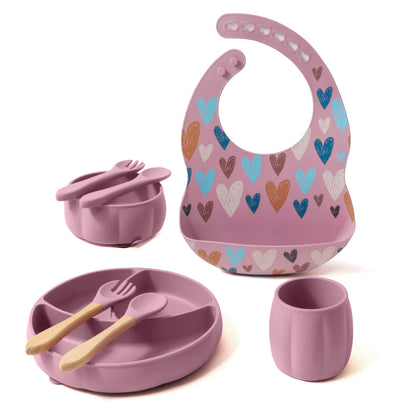 Children's dining set with pink bib, bowl, cup, and utensils on a white background