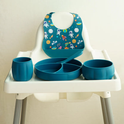 Children's dining set with blue tray, cups, and bib on a high chair against a beige background
