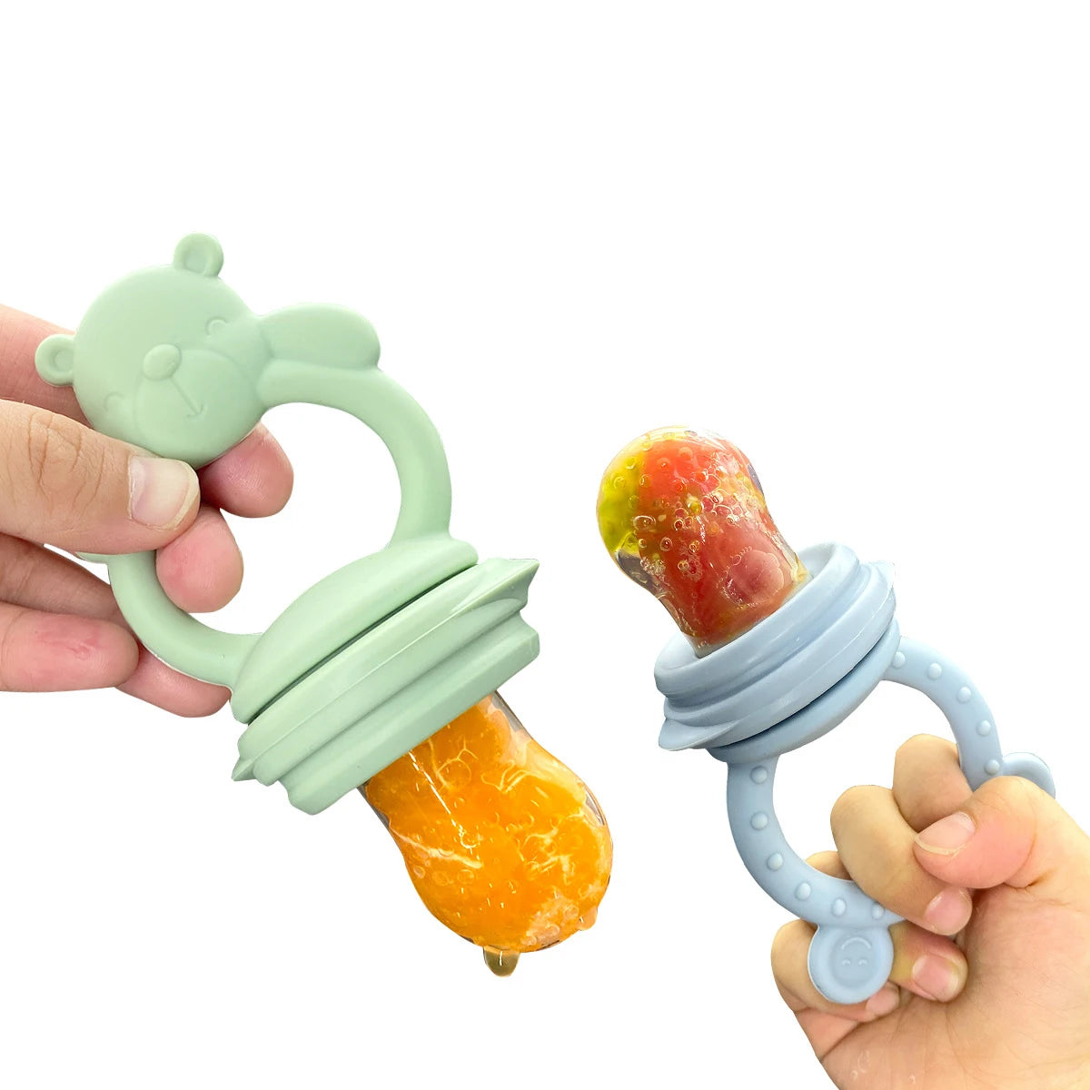 Two baby teething toys with fruit inside, one green and one blue, held by hands against a white background.