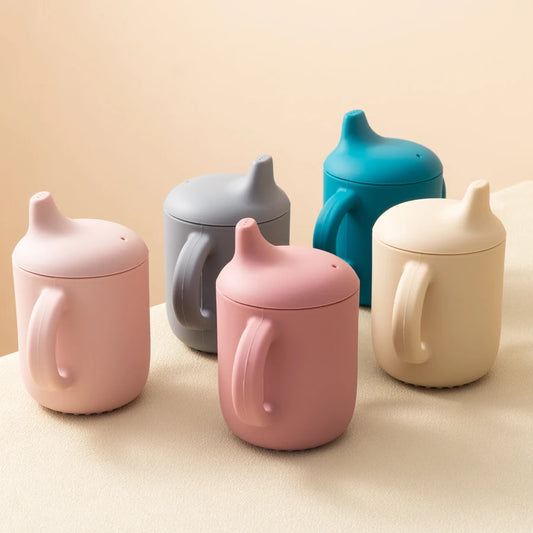 Set of colorful sippy cups on a beige surface
