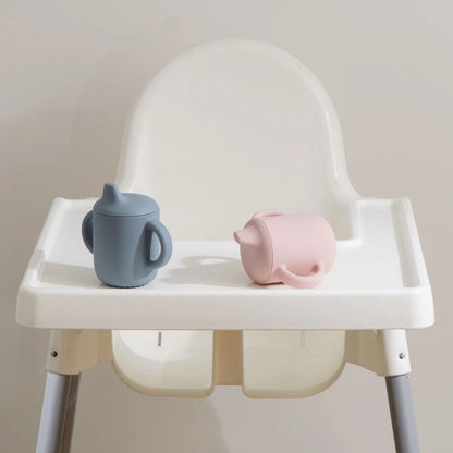 White high chair with a blue sippy cup and pink piggy bank on a neutral background