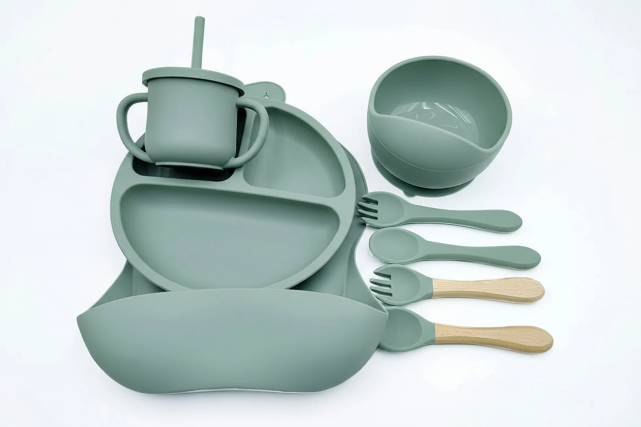 Set of green silicone dining utensils including a cup, bowl, and cutlery on a white background.