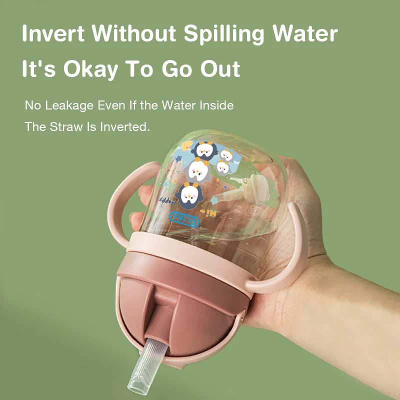 Pink sippy cup with cartoon characters held by a hand against a green background