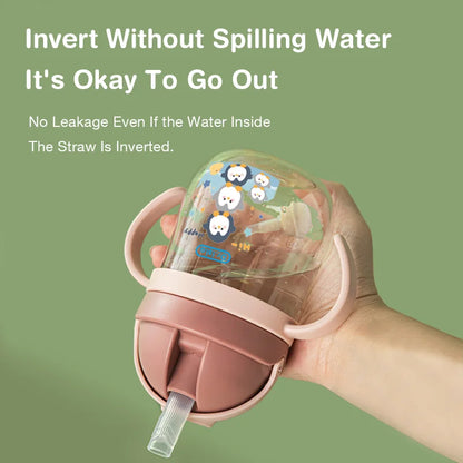 Pink sippy cup with cartoon characters held by a hand against a green background